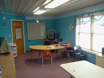 Blue-walled Academy classroom with tables and chairs in 2012.